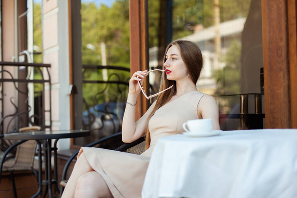 Μια όμορφη γυναίκα κάθεται μόνη της σε ένα τραπέζι στο υπαίθριο καφέ. - Φωτογραφία, εικόνα