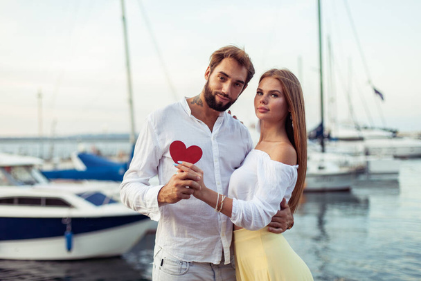Jeune couple amoureux tenant coeur rouge montrant leur amour dans un yacht club, concept romantique - Photo, image