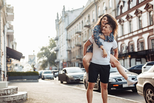 Couple in love. Man carrying girl on his back in the street. Smiling man with beautiful young woman, ride piggyback, having fun together. Relationship concept. - Foto, imagen