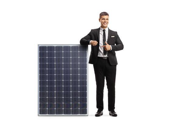 Full length portrait of a professional man in suit and tie leaning on a solar panel and pointing isolated on white background - 写真・画像