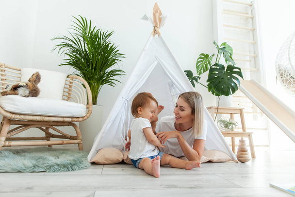 Young mother and little daughter spend time together in a wigwam at home - Foto, afbeelding
