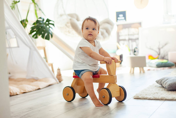 Little girl on a wooden scooter in the children's room - Фото, зображення