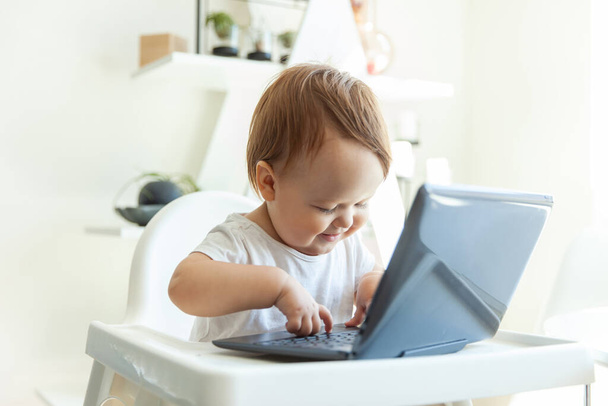 Little funny baby girl typing on a netbook while sitting at the children's table at home - Fotoğraf, Görsel