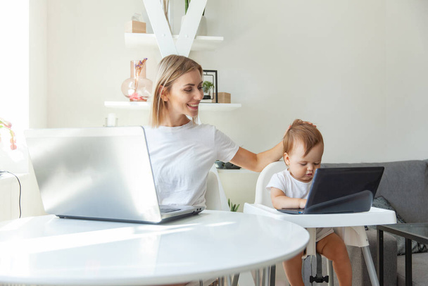 Mom and her little daughter use laptops and sit at the tables at home. Maternity, work and maternity - Foto, Imagem