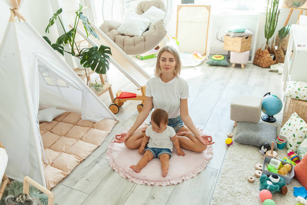 Молодая мама проводит время со своей маленькой девочкой, медитируя дома в позе лотоса. Расслабиться и преодолеть стресс - Фото, изображение