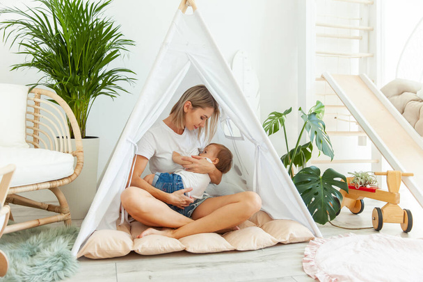 Mom lulls little baby daughter while sitting in a hut in the playroom - Photo, image