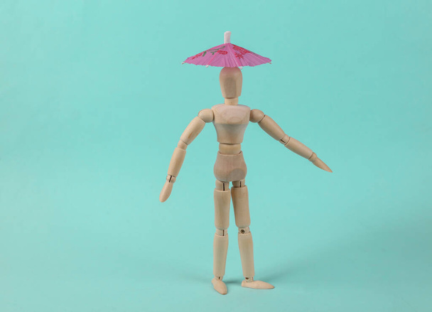 Wooden puppet with umbrella on a blue background. Sun protection - Photo, Image