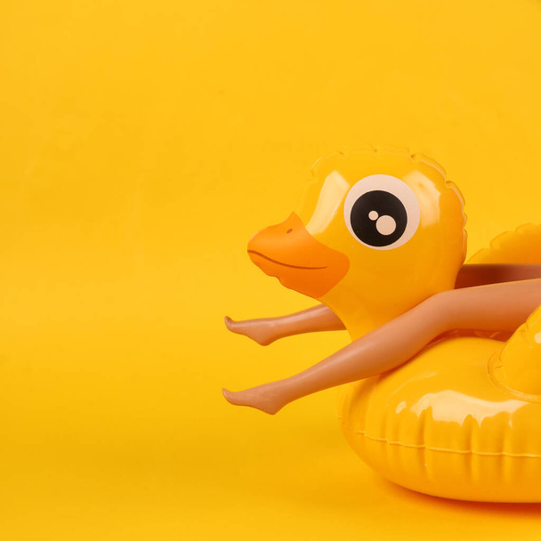 Puppe auf aufblasbarer Ente auf gelbem Hintergrund. Minimales Sommerferienkonzept - Foto, Bild