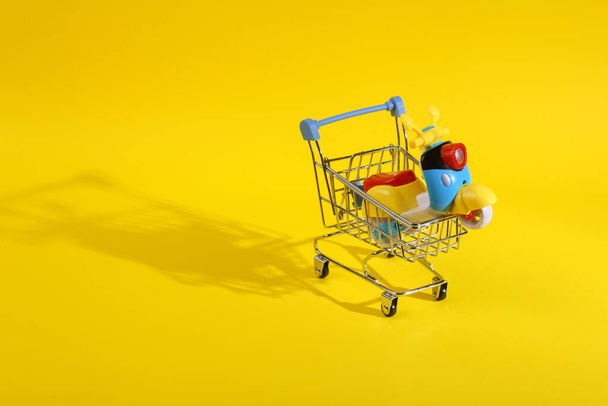 Winkelwagen met scooter model op een gele achtergrond. Korting en verkoop concept - Foto, afbeelding
