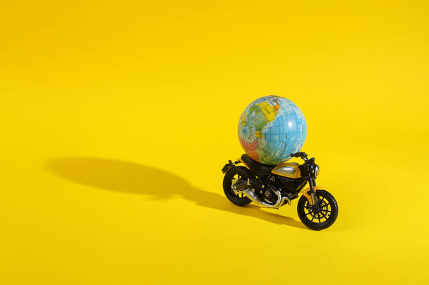 Toy motorcycle with globe on a yellow background with a shadow. Minimal layout. Trip around the world - Photo, image