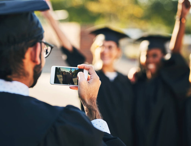 Memories from the big day. Shot of a group of students taking pictures with a mobile phone on graduation day. - Фото, зображення