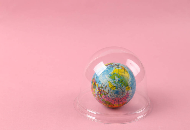 Globe under transparent dome on pink background. Protection, isolation concept. Minimal layout - Photo, Image