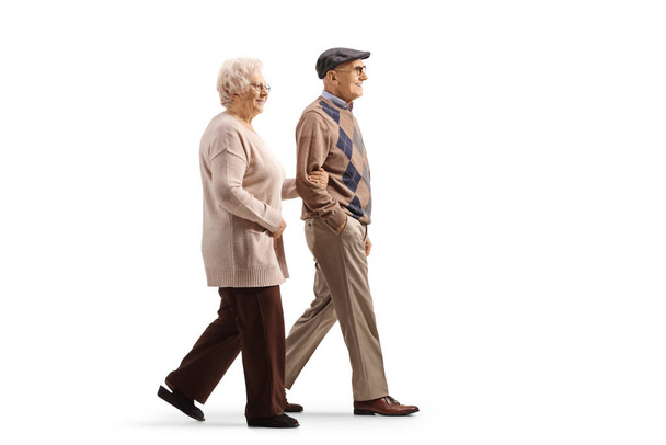 Full length profile shot of an elderly man and woman walking hand in hand isolated on white background - Foto, Bild