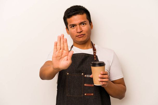 Restaurante camarero hispano sosteniendo un café para llevar aislado sobre fondo blanco de pie con la mano extendida mostrando señal de stop, lo que le impide. - Foto, Imagen