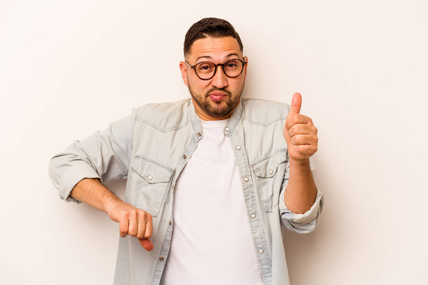 Young hispanic man isolated on white background showing thumbs up and thumbs down, difficult choose concept - Фото, зображення