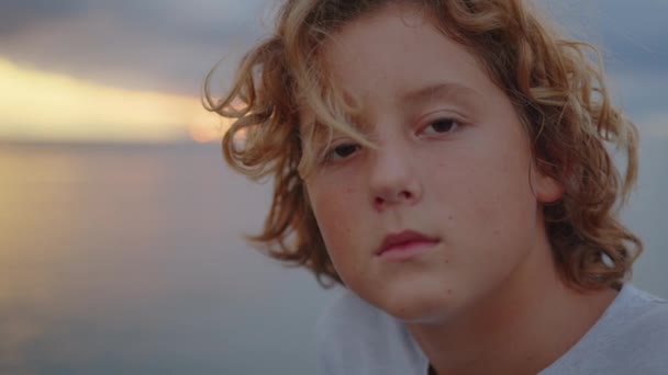 Aantrekkelijke jongen kijkt naar de camera tegen de achtergrond van een prachtige zonsondergang. Close-up - Video