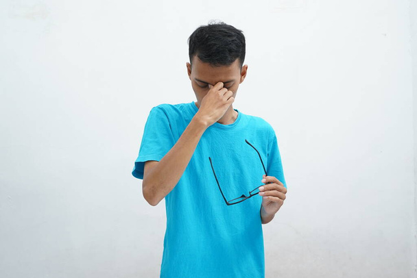 Asiatischer Mann nimmt Nasenmassagebrille ab, Augen haben verschwommenes Sehen, ungesunder Mann leidet unter starken Kopfschmerzen, Schwindel, Sehstörungen. - Foto, Bild