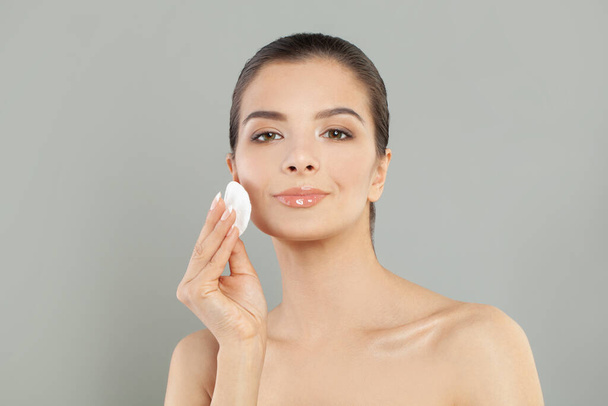 Healthy fresh woman removing makeup from her face with cotton pad. Beauty woman cleaning her face with cotton swab pad isolated on grey background. Skin care and beauty concept. - Photo, Image