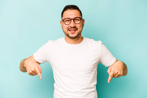 Young hispanic man isolated on blue background points down with fingers, positive feeling. - Foto, afbeelding