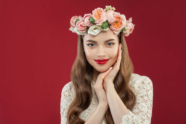Aranyos mosolygós nő nyáron rózsa koszorú portré. Vidám modell virágokkal a piros fal háttér - Fotó, kép