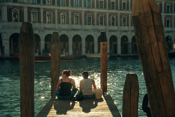 Giovani viaggiatori di sesso femminile seduti sul molo e godendo di una splendida vista sul tramonto a Venezia, Italia - dic, 2021 - Foto, immagini