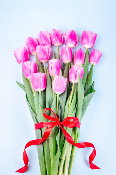 Bunch of beautiful pink white tulips with red ribbon on blue background, vertical, top view - Fotoğraf, Görsel