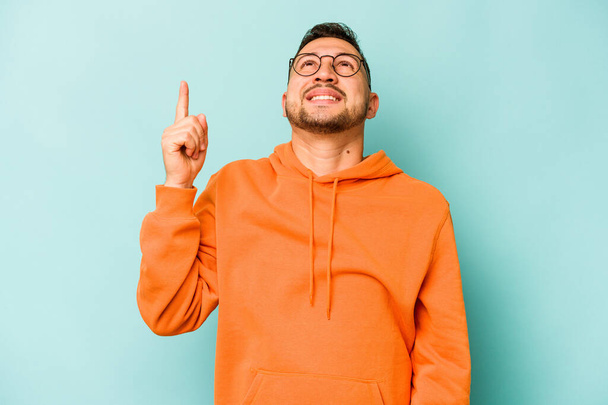 Young hispanic man isolated on blue background indicates with both fore fingers up showing a blank space. - Photo, Image
