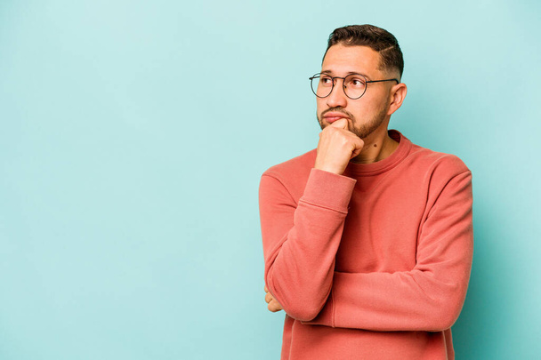 Young hispanic man isolated on blue background looking sideways with doubtful and skeptical expression. - Foto, afbeelding