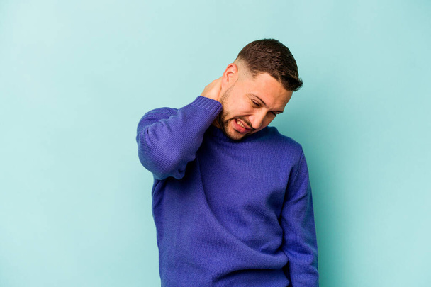 Νεαρός ισπανόφωνος άνδρας απομονωμένος σε μπλε φόντο που υποφέρει από πόνο στο λαιμό λόγω καθιστικού τρόπου ζωής. - Φωτογραφία, εικόνα