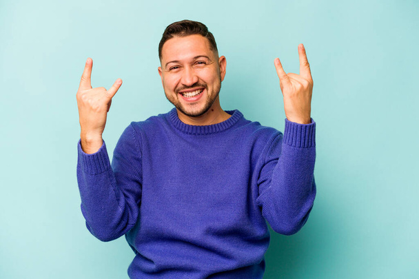 Young hispanic man isolated on blue background showing a horns gesture as a revolution concept. - Фото, изображение