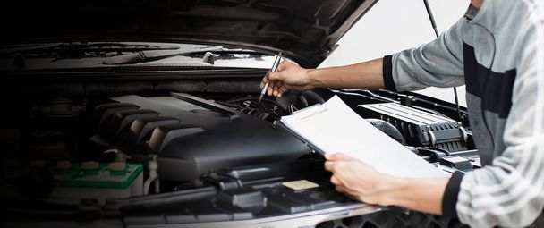 Automekaanikko tarkistaa auton moottorin tarkastamalla kirjallisesti leikepöydälle tarkistuslistan korjaus kone, auton huolto ja huolto. - Valokuva, kuva