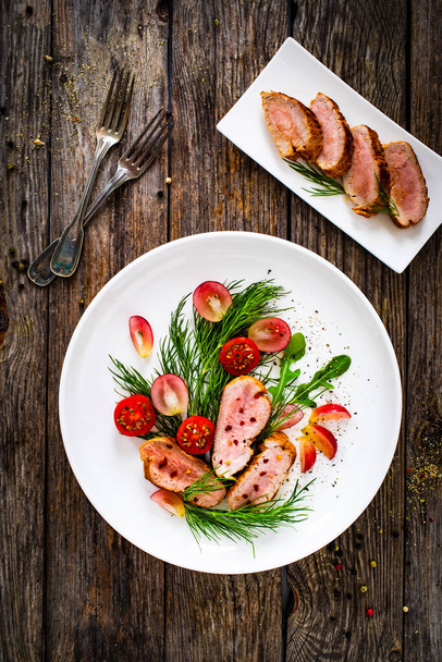 Roasted pork loin slices with dill and cherry tomatoes on wooden table - Фото, изображение