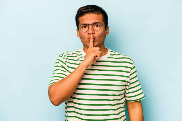 Young hispanic man isolated on blue background keeping a secret or asking for silence. - Photo, Image