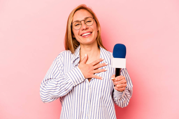 Jovem caucasiano apresentador de TV mulher isolada no fundo rosa ri em voz alta mantendo a mão no peito. - Foto, Imagem