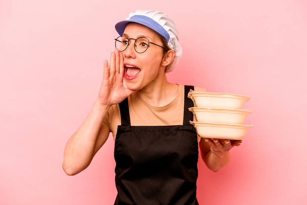 Giovane cuoco volontario donna isolato su sfondo rosa gridando e tenendo palmo vicino bocca aperta. - Foto, immagini