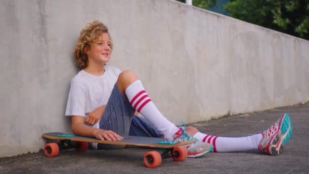 Šťastný teenager, stylový bruslař chlapec drží svůj skateboard venku - Záběry, video