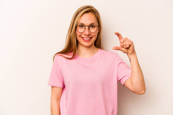 Young caucasian woman isolated on white background holding something little with forefingers, smiling and confident. - Photo, Image