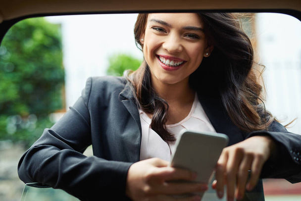 I always plan my day before I get going. Shot of an attractive young businesswoman using a cellphone leaning on the window of a car. - Fotoğraf, Görsel