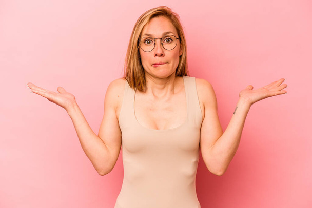 Young caucasian woman isolated on pink background confused and doubtful shrugging shoulders to hold a copy space. - Photo, Image
