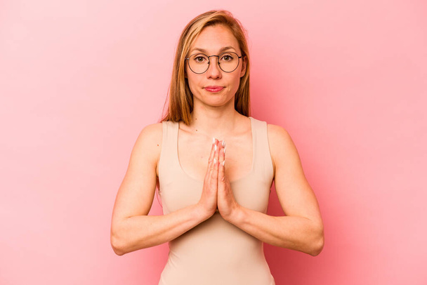 Young caucasian woman isolated on pink background praying, showing devotion, religious person looking for divine inspiration. - Photo, Image