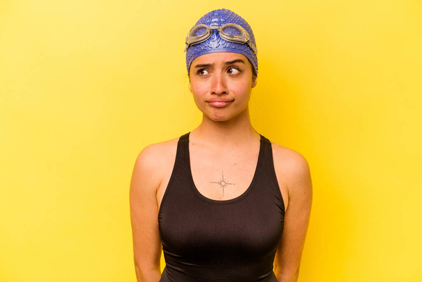 Nuori uimari latino nainen eristetty keltaisella taustalla sekava, tuntuu epäilyttävältä ja epävarma. - Valokuva, kuva