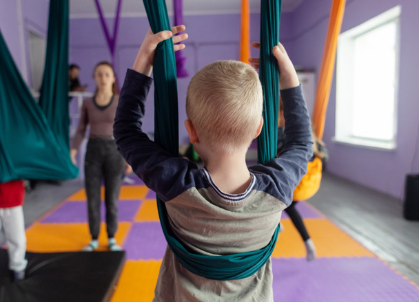 Fly yoga for children. Kids and the coach are doing aerial acrobatics on cloth canvases. Parents and children train in hammocks. Air gymnastics. - Photo, image