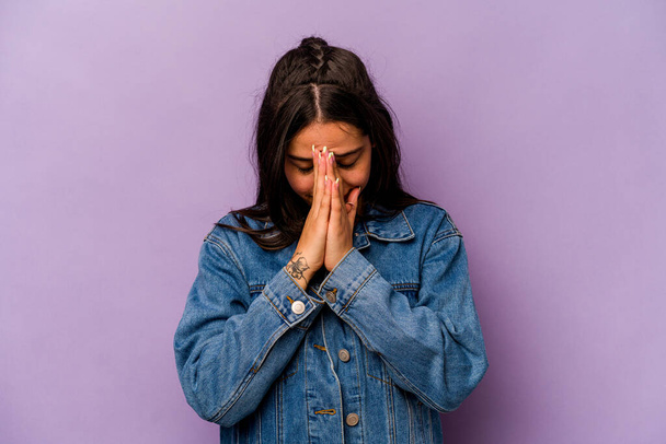 Junge hispanische Frau isoliert auf lila Hintergrund betet, zeigt Hingabe, religiöse Person auf der Suche nach göttlicher Inspiration. - Foto, Bild