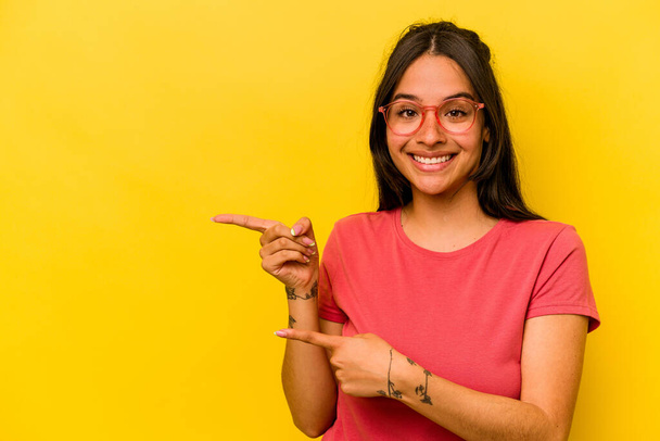 Young hispanic woman isolated on yellow background excited pointing with forefingers away. - Foto, Imagen
