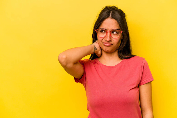Junge hispanische Frau isoliert auf gelbem Hintergrund berührt Hinterkopf, denkt nach und trifft eine Wahl. - Foto, Bild