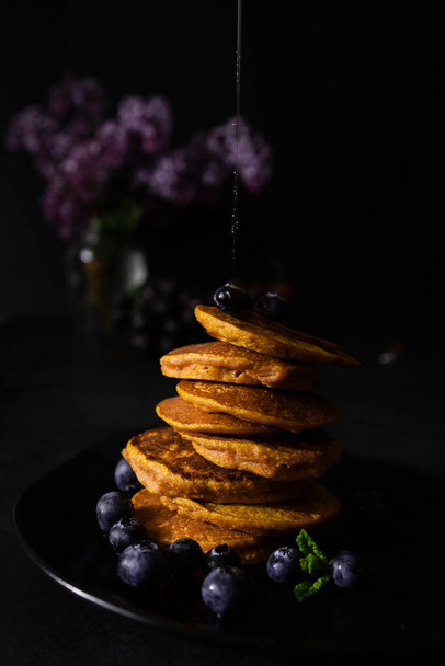 Zelfgemaakte pannenkoeken met ahornsiroop en verse bosbessen. Zelfgemaakt en gezond ontbijt met donkere achtergrond. Glutenvrije wortelpannenkoeken - Foto, afbeelding