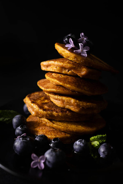 Zelfgemaakte pannenkoeken met ahornsiroop en verse bosbessen. Zelfgemaakt en gezond ontbijt met donkere achtergrond. Glutenvrije wortelpannenkoeken - Foto, afbeelding