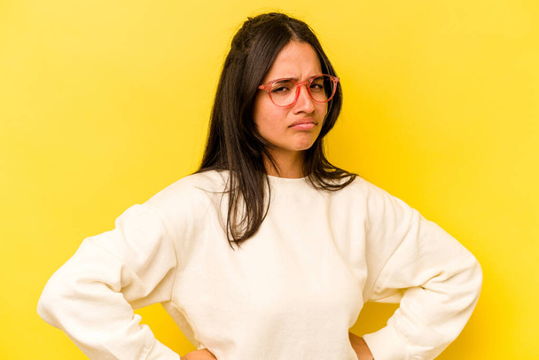 Young hispanic woman isolated on yellow background frowning face in displeasure, keeps arms folded. - Photo, Image