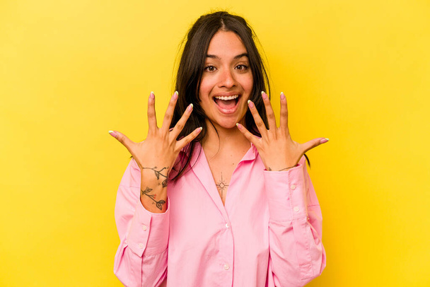 Junge hispanische Frau isoliert auf gelbem Hintergrund, die Nummer zehn mit Händen zeigt. - Foto, Bild
