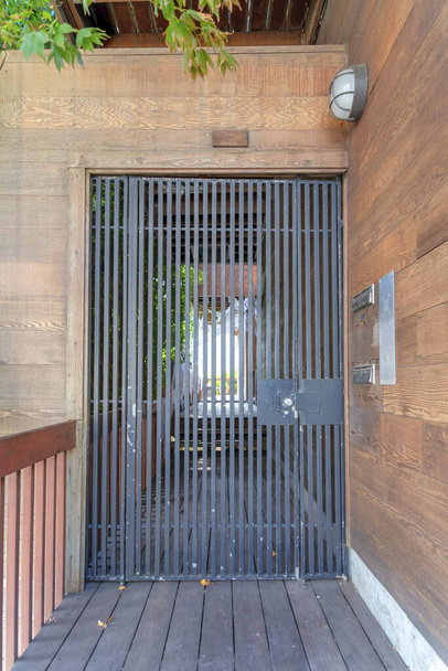 Puerta de hierro forjado con paredes de tablones de madera y camino en San Francisco, California. Entrada de una casa con rejas a la izquierda a través de la pared de madera con dos buzones montados en la pared a la derecha. - Foto, Imagen
